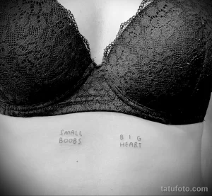 Черно-белое фото татуировки с надписями 'Small boobs' и 'Big heart' под кружевным бюстгальтером на женской груди. Минималистичный рисунок тату.