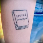 Фото татуировки на руке с изображением книги 'Little Women'. Простой рисунок, тонкие линии, черно-белое изображение.