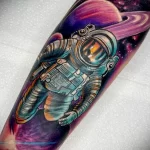 цветной рисунок татуировки на руке с космонавтом в открытом космосе