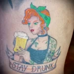 Фото тату с изображением рыжеволосой девушки с кружкой пива и надписью "Stay Drunk". Яркий рисунок в традиционном стиле.