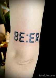 Фото татуировки на предплечье с надписью 'BEER', выполненной в стиле цифрового шрифта. Черно-белый рисунок с четкими линиями и минималистичным дизайном.