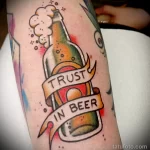 Фото тату: татуировка бутылки пива с надписью "Trust in Beer", выполненная в стиле олдскул. Цветная татуировка с четкими контурами и традиционными элементами.