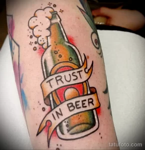 Фото тату: татуировка бутылки пива с надписью "Trust in Beer", выполненная в стиле олдскул. Цветная татуировка с четкими контурами и традиционными элементами.