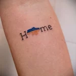Фото татуировки с надписью 'Home' и изображением гор, выполненной на руке. Минималистичный рисунок татуировки символизирует любовь к дому и природе.