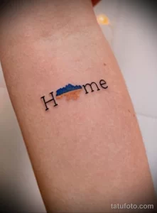 Фото татуировки с надписью 'Home' и изображением гор, выполненной на руке. Минималистичный рисунок татуировки символизирует любовь к дому и природе.