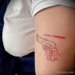 Небольшая татуировка на предплечье с изображением пистолета и надписью на украинском языке 'Скажи Паляница'. Минималистичный рисунок татуировки.