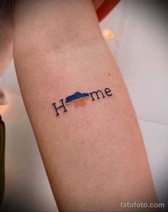 Фото татуировки с надписью "Home" и изображением карты Украины внутри буквы "o" на руке, выполненной в минималистичном стиле.