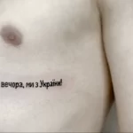Фото татуировки с надписью на украинском языке "Доброго вечора, ми з України!" на груди, выполненной черным цветом.