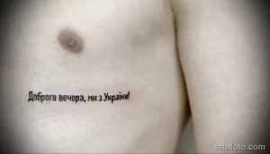 Фото татуировки с надписью на украинском языке "Доброго вечора, ми з України!" на груди, выполненной черным цветом.