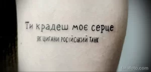 Фото татуировки с надписью на украинском языке "Ти крадеш моє серце як цигани російський танк" на руке, выполненной черным цветом.