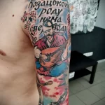Фото тату на руке: красочный портрет козака, играющего на бандуре, окруженного цветами и лентами. Детализированный рисунок татуировки.