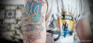 Фото татуировки на руке: украинский флаг, герб, надпись 'Смерть ворогам' и военные символы. Яркие цвета и детализированная проработка.