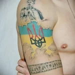 Фото татуировки на плече с изображением казака, украинского флага и надписи 'Слава Україні!'. Яркий и красочный рисунок татуировки.