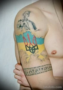Фото татуировки на плече с изображением казака, украинского флага и надписи 'Слава Україні!'. Яркий и красочный рисунок татуировки.