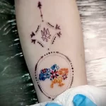 Фото татуировки на руке с изображением карты Украины, заключенной в круг, стилизованного трезубца и стрелы, символизирующей направление и защиту. Яркий рисунок татуировки.
