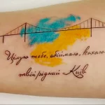 Фото тату: мост, стилизованный под флаг Украины, и романтическая надпись на коже. Красивый рисунок татуировки в акварельном стиле.