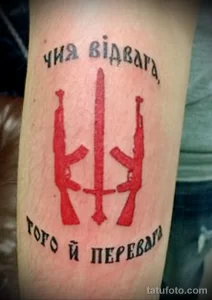 Фото тату: две винтовки и надпись на украинском языке на предплечье. Патриотический рисунок татуировки в красных тонах.