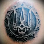 Фото тату: стилизованный трезубец Украины в круге, выполненный в технике blackwork. Лаконичный рисунок татуировки на коже.