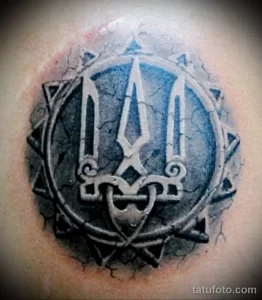 Фото тату: стилизованный трезубец Украины в круге, выполненный в технике blackwork. Лаконичный рисунок татуировки на коже.