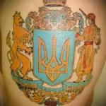 Фото тату на руке: Герб Украины в стиле барокко с короной, львом и казаком. Цветной рисунок татуировки.