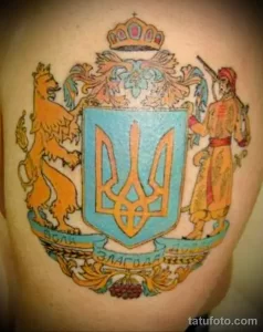 Фото тату на руке: Герб Украины в стиле барокко с короной, львом и казаком. Цветной рисунок татуировки.