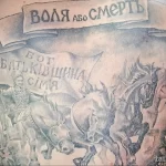 Фото тату на груди с изображением казаков верхом на лошадях и надписями на украинском языке. Детализированный рисунок в серо-черных тонах.