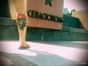 Фото тату сердца с украинским тризубом на ноге. Яркий рисунок татуировки в стиле традиционной татуировки с использованием синих и желтых цветов.