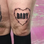 Фото татуировки колючей проволоки в форме сердца с надписью 'BABY' на колене. Черно-белый рисунок, выполненный в графическом стиле.
