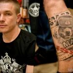 Фото тату на руке, изображающее медведя в ушанке. Детализированный рисунок татуировки с использованием черно-белой гаммы и реалистичной проработкой деталей.