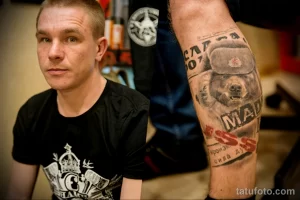 Фото тату на руке, изображающее медведя в ушанке. Детализированный рисунок татуировки с использованием черно-белой гаммы и реалистичной проработкой деталей.