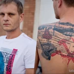 Фото тату на спине, изображающее советскую агитационную графику с элементами плакатов и текстов. Детализированный рисунок татуировки с использованием черно-красной гаммы.
