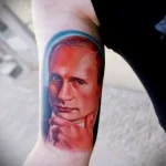 Фото тату: реалистичный портрет Владимира Путина на предплечье, выполненный в цвете с использованием голубого ореола вокруг головы.