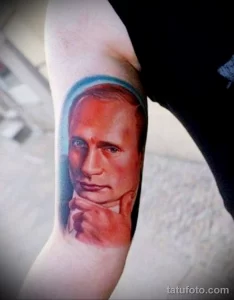 Фото тату: реалистичный портрет Владимира Путина на предплечье, выполненный в цвете с использованием голубого ореола вокруг головы.