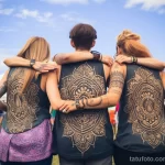 Фотография группы девушек с татуировками на спине, обнимающихся на фоне голубого неба и зеленой травы. Идеально для поиска идей для тату на спине.