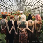 Фотография группы девушек с татуировками на спине, стоящих спиной к камере в теплице, окруженных цветами. Идеально для поиска идей для тату на спине.