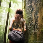 A woman revealing an intricate tattoo of an ancient tree on her side, while hiking in a majestic forest 4 - 07,11,2023 tatufoto.com