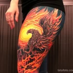 A woman with a detailed thigh tattoo of a mythical phoenix, posing in front of a dramatic fiery backdrop 3 - 07,11,2023 tatufoto.com