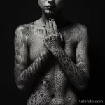 Фотография женщины с полностью покрытым татуировками телом. Сложный геометрический орнамент в стиле трайбл, охватывающий все тело, включая лицо и руки.