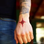 Фото минималистичной татуировки на руке, изображающей символ охотника из игры Bloodborne, выполненный в красном цвете с четкими линиями. Стильный и лаконичный дизайн.