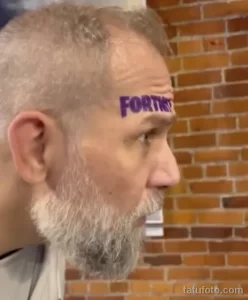 Фотография мужчины с татуировкой 'FORTNITE' на лбу. Мужчина смотрит в сторону, на лице выражение задумчивости.