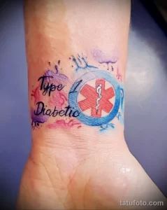 Фото тату на запястье: надпись 'Type 1 Diabetic' в акварельной технике с голубым медицинским крестом. Нежный и выразительный рисунок.
