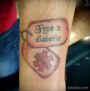 Фото тату на предплечье: красный медицинский крест и надпись 'Type 2 diabetic' в черном контуре. Идентификационная татуировка для людей с диабетом.