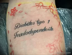 Фото татуировки на руке с надписью 'Diabetes tipo 1 Insulodependiente' и небольшими цветочными элементами. Черно-серый рисунок татуировки.