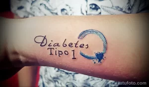 Фото тату надписи 'Diabetes Tipo 1' с небольшим синим полумесяцем на предплечье. Минималистичный стиль, черные чернила, акцент на значимости здоровья.