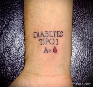 Фото тату: надпись 'Diabetes Tipo 1 A+' и изображение капли крови на запястье, выполненные в черном цвете.