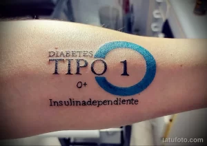 Фото тату: надпись 'Diabetes Tipo 1' в круге, выполненная в сочетании черных и голубых чернил на руке.