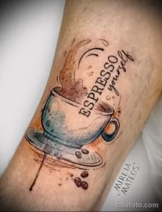 Фото тату чашки эспрессо с паром и надписью 'Espresso yourself' на предплечье в стиле акварель и графика, с кофейными зернами.