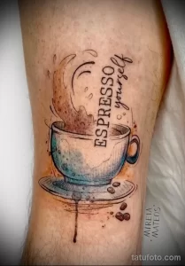Фото тату чашки эспрессо с паром и надписью 'Espresso yourself' на предплечье в стиле акварель и графика.
