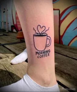 Фото татуировки на лодыжке с изображением чашки кофе и надписью 'Morning Coffee'. Простой и минималистичный рисунок татуировки.