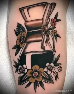 Фото татуировки на руке с изображением кофеварки, украшенной цветами. Стиль олдскул, яркие цвета, четкие контуры.